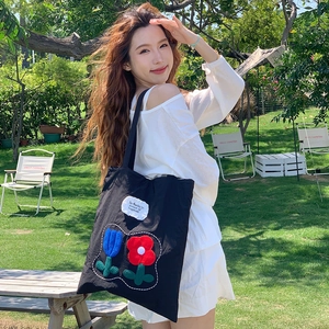 Detail of black nylon tote bag featuring colorful tulip embroidery and white patch label