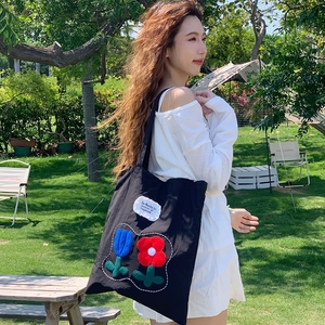 Close-up of black canvas tote bag featuring floral embroidery and patch detail in nature