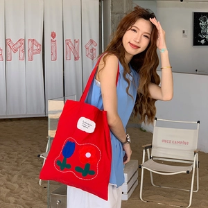 Detail of red canvas tote bag featuring floral tulip embroidery and durable straps