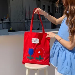 Detail of red canvas tote bag with floral embroidery and ruffle trim slogan patch