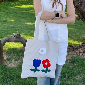 Detail of floral tulip embroidery and text label on a white nylon tote bag