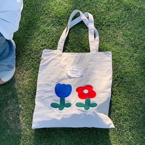 Close-up of beige canvas tote with embroidered blue and red flowers on a sunny lawn