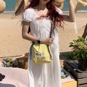 Détail d'un sac bandoulière en toile jaune avec broderie sur une plage ensoleillée