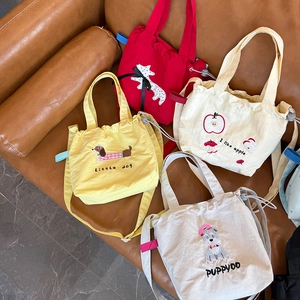 Detail of four colorful canvas crossbody bags with animal and fruit embroidery on a sofa