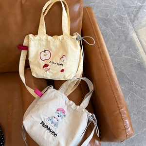 Detail view of canvas crossbody bags with apple and puppy embroidery on a leather sofa