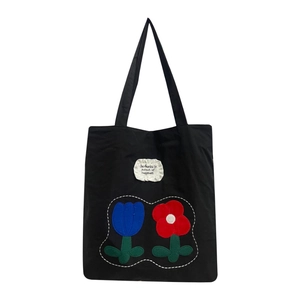 Minimalist black nylon tote bag with floral embroidery and ruffle tag on white background