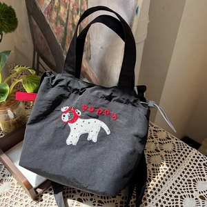 Detail of black nylon drawstring bag featuring puppy embroidery and red decorative strap
