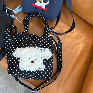 Detail of cute puppy embroidery and blue bow on black polka dot canvas crossbody bag