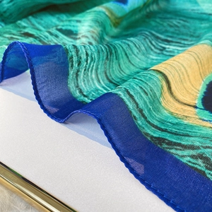 Close-up of silk scarf with vibrant peacock feather pattern and fine blue stitched edges