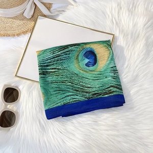 Detail of peacock feather print on silk-like green scarf with luxury texture