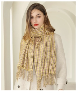 Détail d'une écharpe à carreaux jaunes avec de longues franges sur un manteau blanc