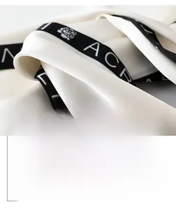 Macro shot of white silk twill scarf with black jacquard ribbon and letter pattern