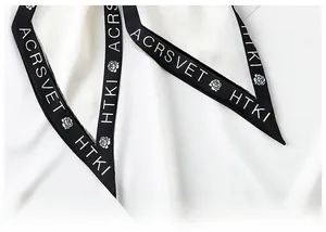 Close-up of white silk scarf showing black floral print and fine edge stitching detail