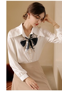 Close-up of elegant long silk scarf with letter print styled as a bow on a white blouse