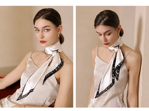 Detail of elegant cream silk scarf with black borders and letter print on textured fabric