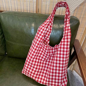Classic red and white gingham cotton tote bag displayed on a dark green leather sofa