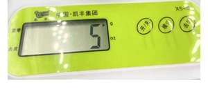 Close-up of kitchen scale LCD display showing 5g unit and green control panel buttons