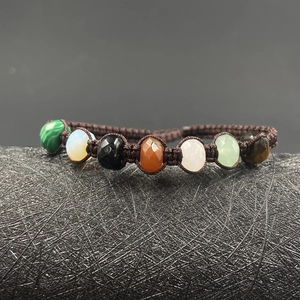 Handwoven natural crystal bracelet with seven colorful gemstones on a dark stand