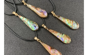 Set of five teardrop abalone shell necklaces with golden edges on a dark surface
