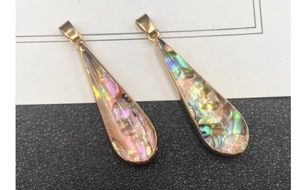 Macro detail of iridescent abalone shell teardrop pendants with golden metal edges