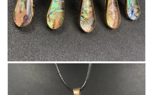 Macro detail of teardrop abalone shell pendant with gold gilded edges and black cord