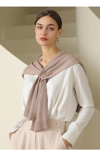 Detail of soft pink knitted shawl draped over cream blouse and camel trousers