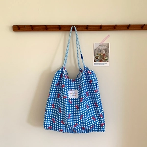 Detail view of plaid tote bag featuring red bow prints and blue rope handles