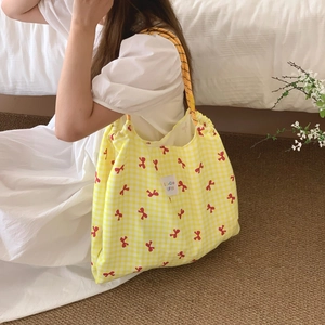 Detail of yellow checkered tote bag with red bows and brand label in home setting