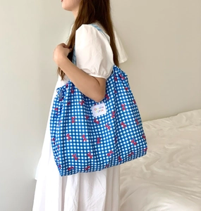 Close-up of a blue plaid tote bag with red bow patterns and a side shoulder strap