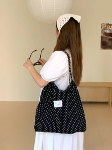 Detail of black polka dot tote bag with white woven label on a model in a minimal room