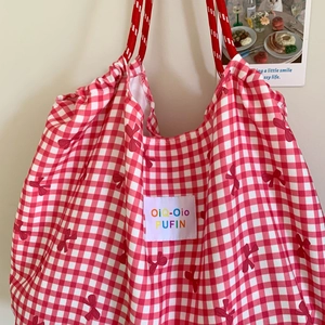 Close-up of red plaid canvas tote bag with bow print and woven rope handles