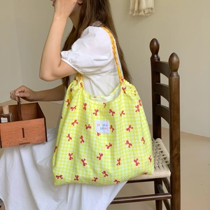 Detail of yellow checkered canvas tote bag with red bow print and woven brand label
