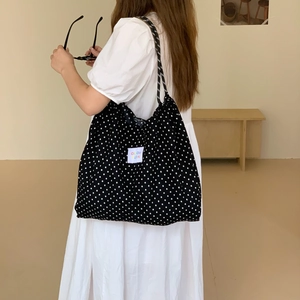 Detail of a large black canvas tote bag with white polka dots and a stylish side-carry view