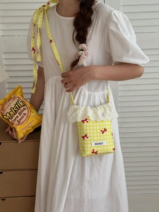 Detail of yellow checkered crossbody bag with red bow print and white lace trim
