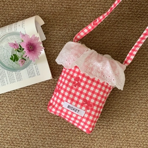 Detail of pink plaid phone bag with red bows, lace trim, and Bisket label on woven rug
