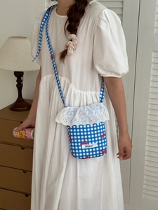 Detail of blue plaid canvas crossbody bag with white lace trim and red bow pattern