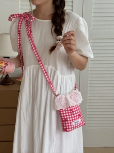 Detail of red gingham crossbody bag with lace embroidery and pink ribbon shoulder strap