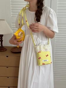 Close-up of a yellow plaid crossbody phone bag with red bows and lace trim details