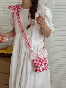 Detail of red gingham crossbody bag with lace trim and bow on white linen dress