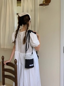 Detail of checkered crossbody bag with white lace trim and dotted strap in cozy interior
