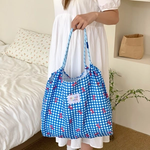 Blue plaid tote bag with pink bow prints and rope handles in a cozy home setting