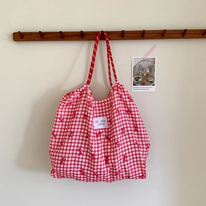 Red checkered canvas tote bag with drawstring detail hanging on a wooden wall hook