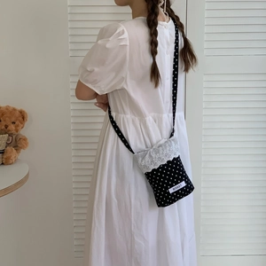 Polka dot mini crossbody bag with white lace trim and bow details on white dress model