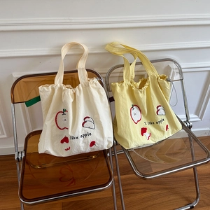 Detailed close-up of canvas tote bags featuring red apple embroidery and drawstring closure