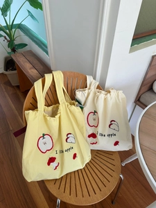 Detail of drawstring canvas tote bags with red apple embroidery on a wooden chair