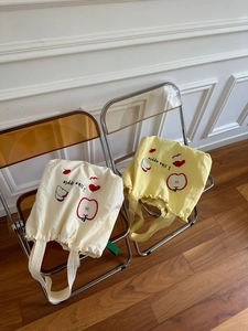 Close-up of canvas tote bag with red apple embroidery and letter print on a stylish chair