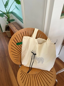 Detail of cream tote bag featuring butterfly bow and green label on wood background