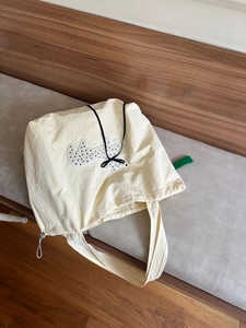 Detail view of cream nylon tote bag featuring dog appliqué and adjustable drawstring design