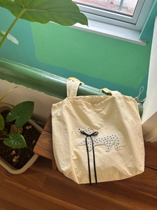 Detail of beige drawstring tote bag featuring a cute polka dot dog patch and black ribbon