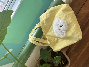 Detail of yellow tote bag featuring a plush puppy patch in a natural outdoor setting